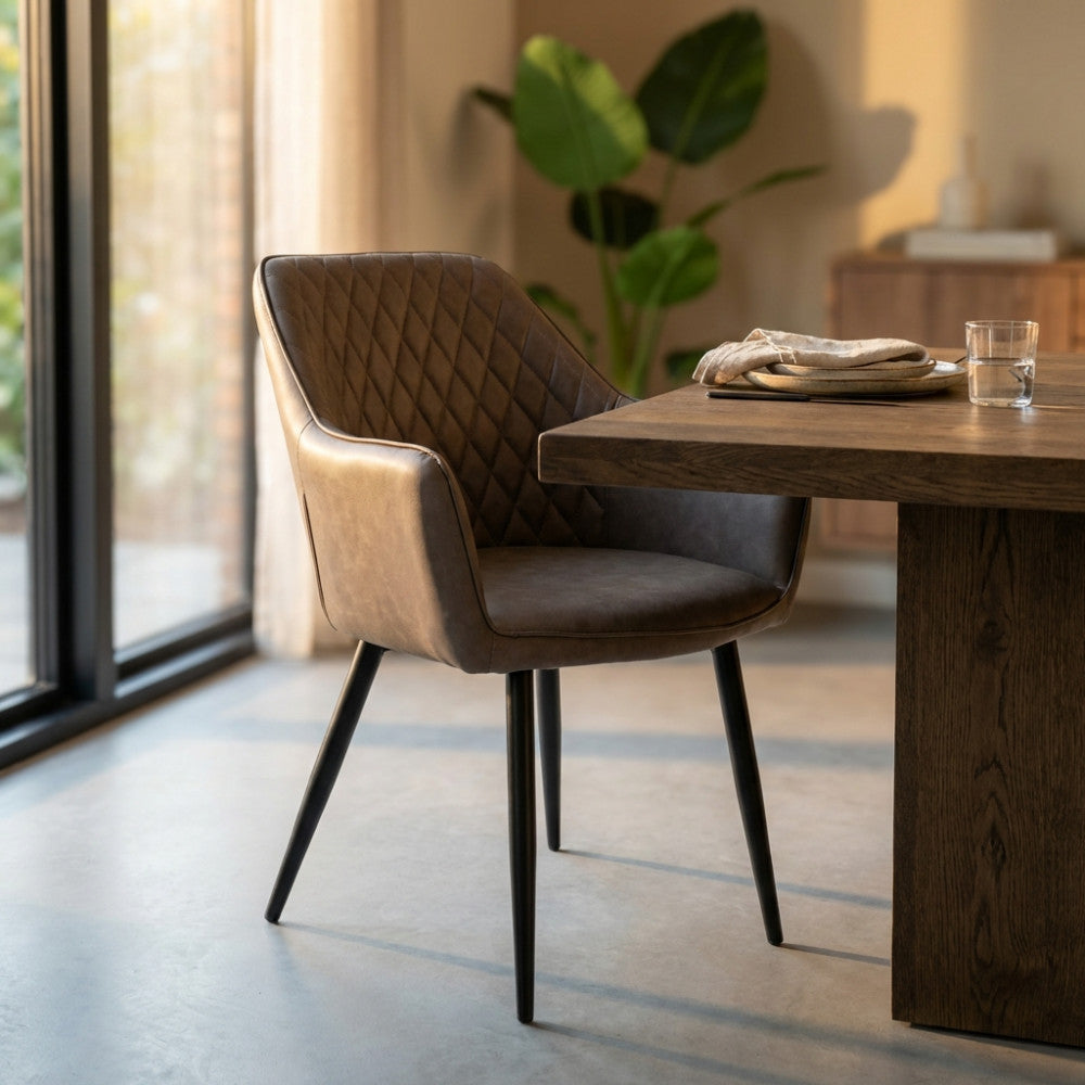 Poltrona Sindy in ecopelle marrone ambientata in una sala da pranzo moderna con tavolo in legno massello e luce naturale.