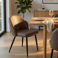 Poltrona Sissy in ecopelle marrone illuminata dalla luce naturale accanto a un tavolo da pranzo in legno.