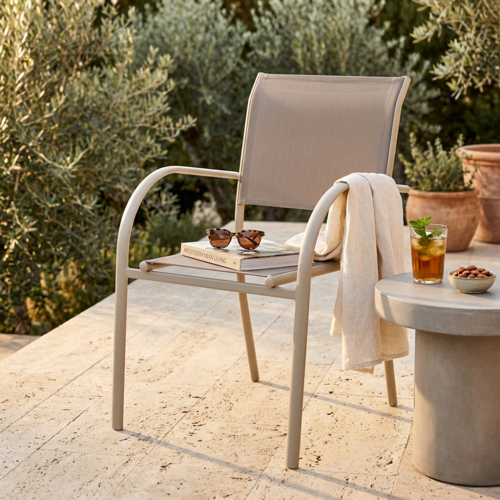 Poltrona Stamford in textilene tortora ambientata su un patio in pietra soleggiato con bevanda rinfrescante e occhiali da sole.