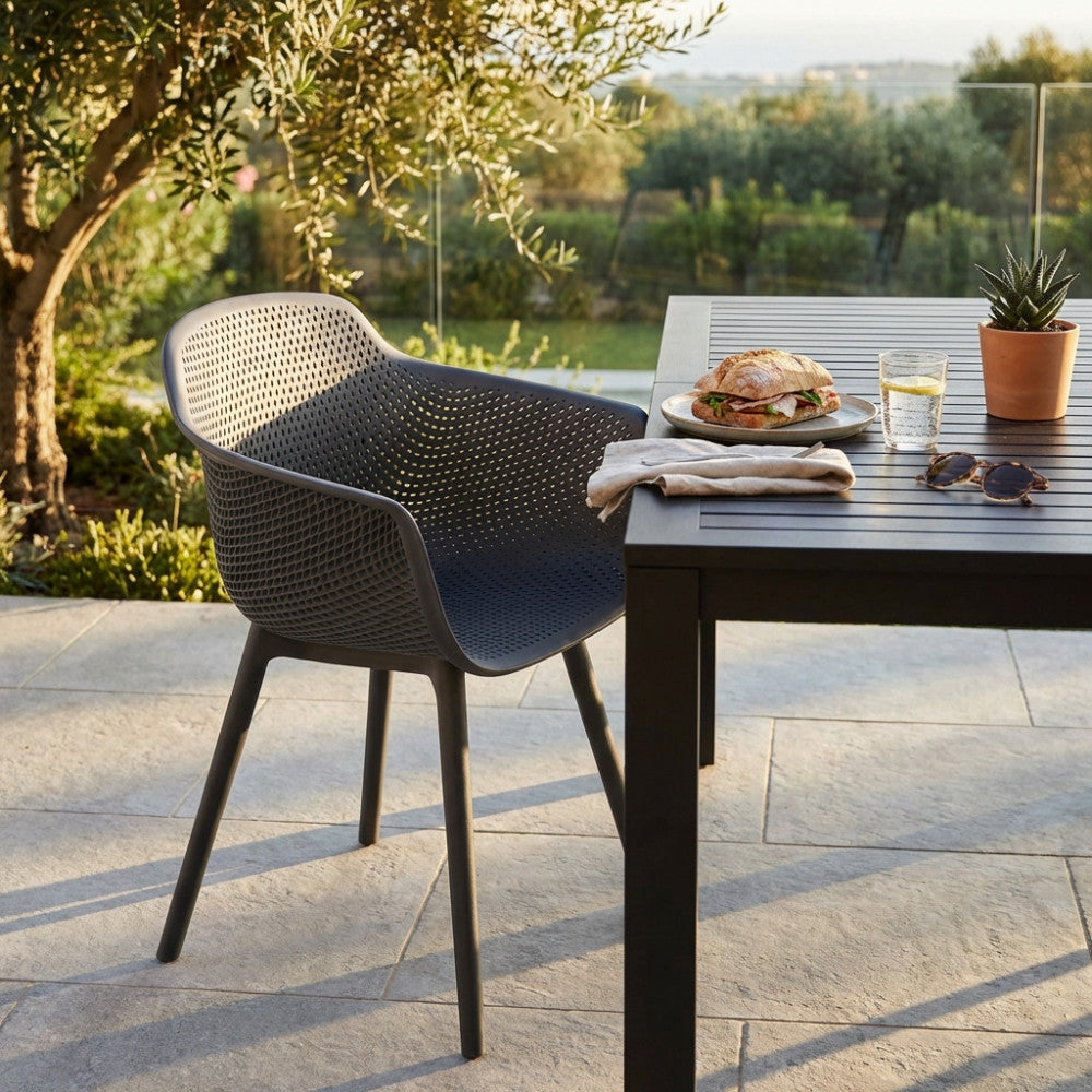 Poltrona Vannes in plastica taupe ambientata all'aperto accanto a un tavolo da pranzo scuro.