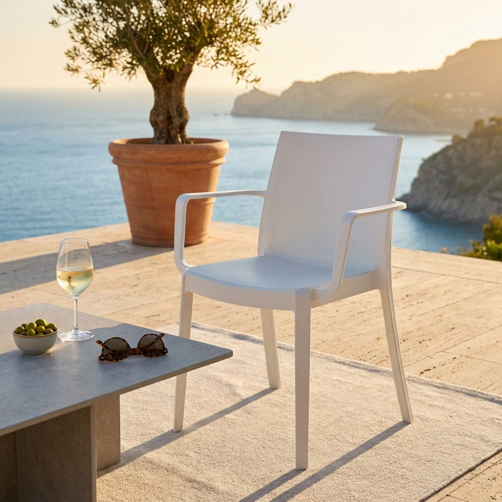 Poltrona Victoria in polipropilene bianco posizionata su una terrazza in pietra con vista mare, accanto a un tavolino con calice di vino.