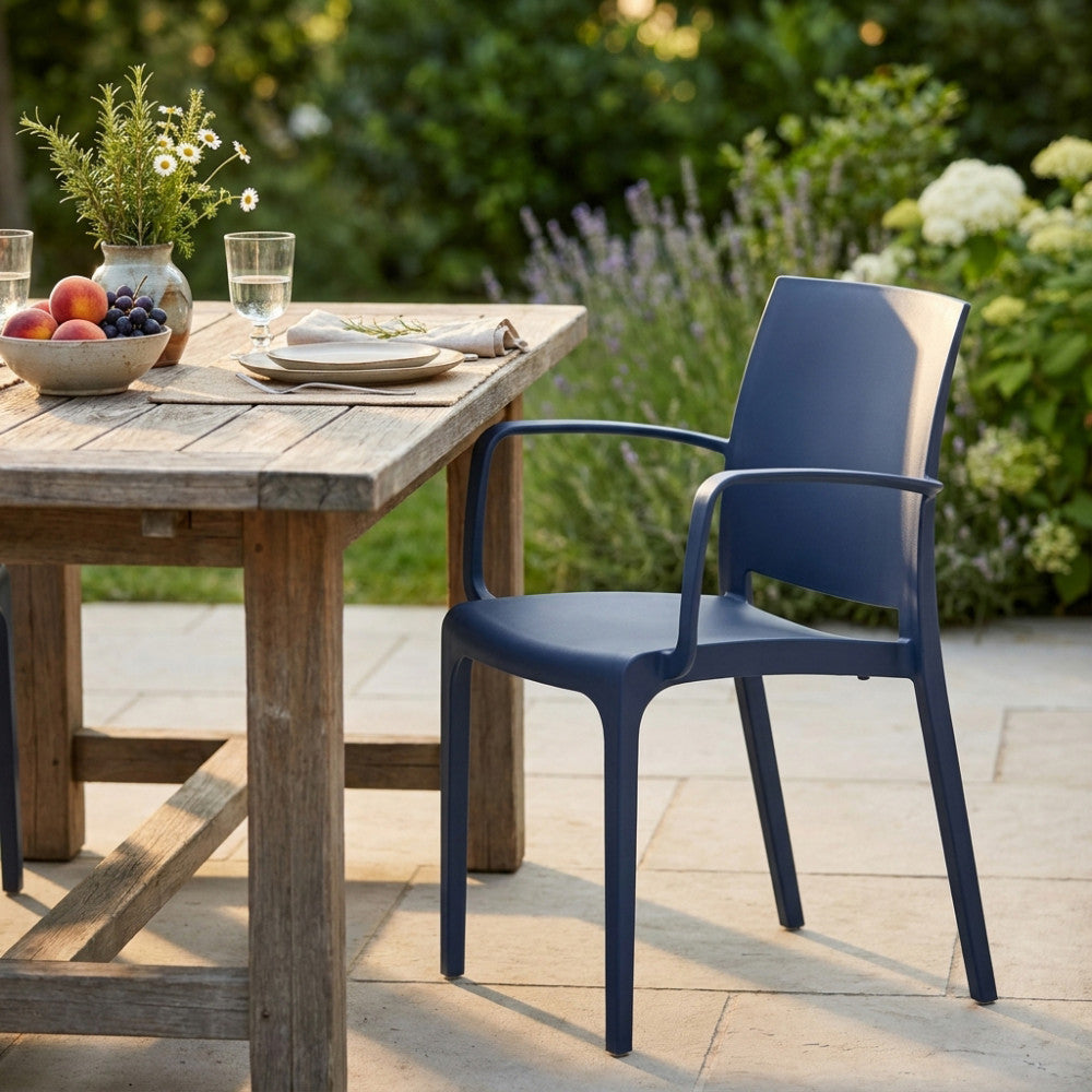 L'elegante poltrona Volga blu abbinata a un tavolo da pranzo in legno rustico con frutta fresca in un rigoglioso giardino.