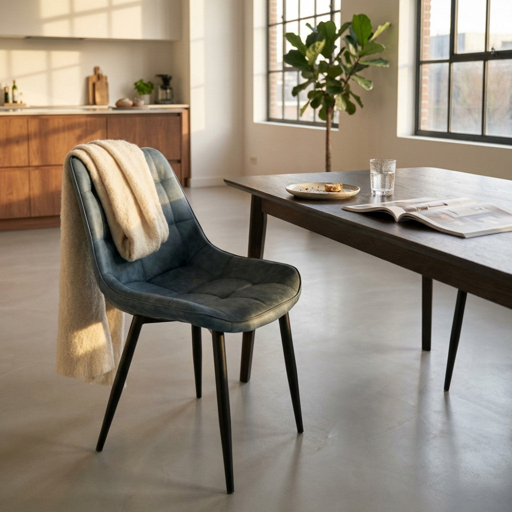 Poltrona moderna blu con coperta chiara appoggiata, in una sala da pranzo luminosa.