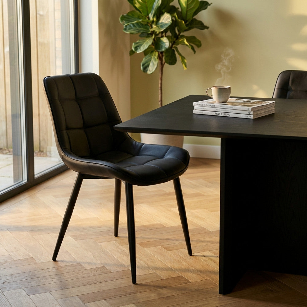 Poltrona Winona in ecopelle nera ambientata in una sala da pranzo moderna con tavolo nero.
