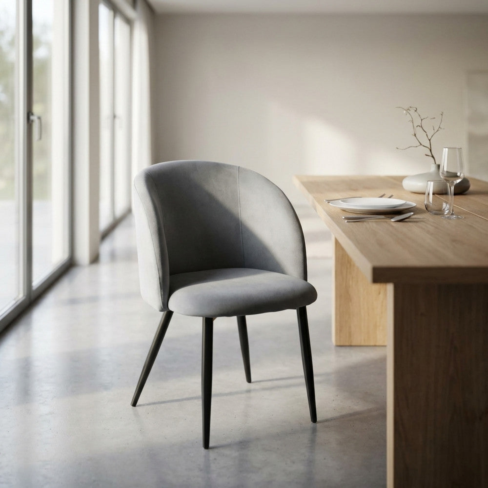 Poltrona Yasmina in velluto grigio accanto a un tavolo da pranzo minimalista in un ambiente luminoso.