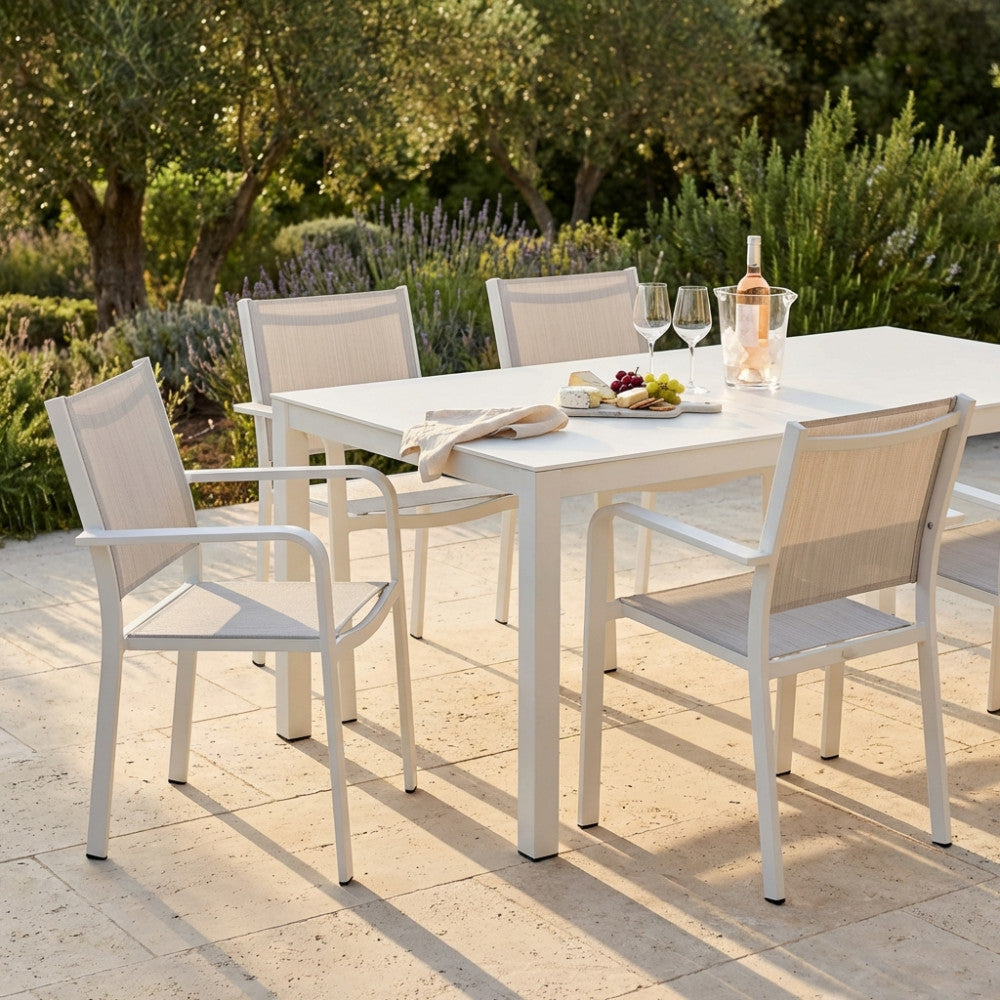 Set da pranzo outdoor con poltrone Zante impilabili attorno a un tavolo bianco, illuminate dalla calda luce del tramonto.