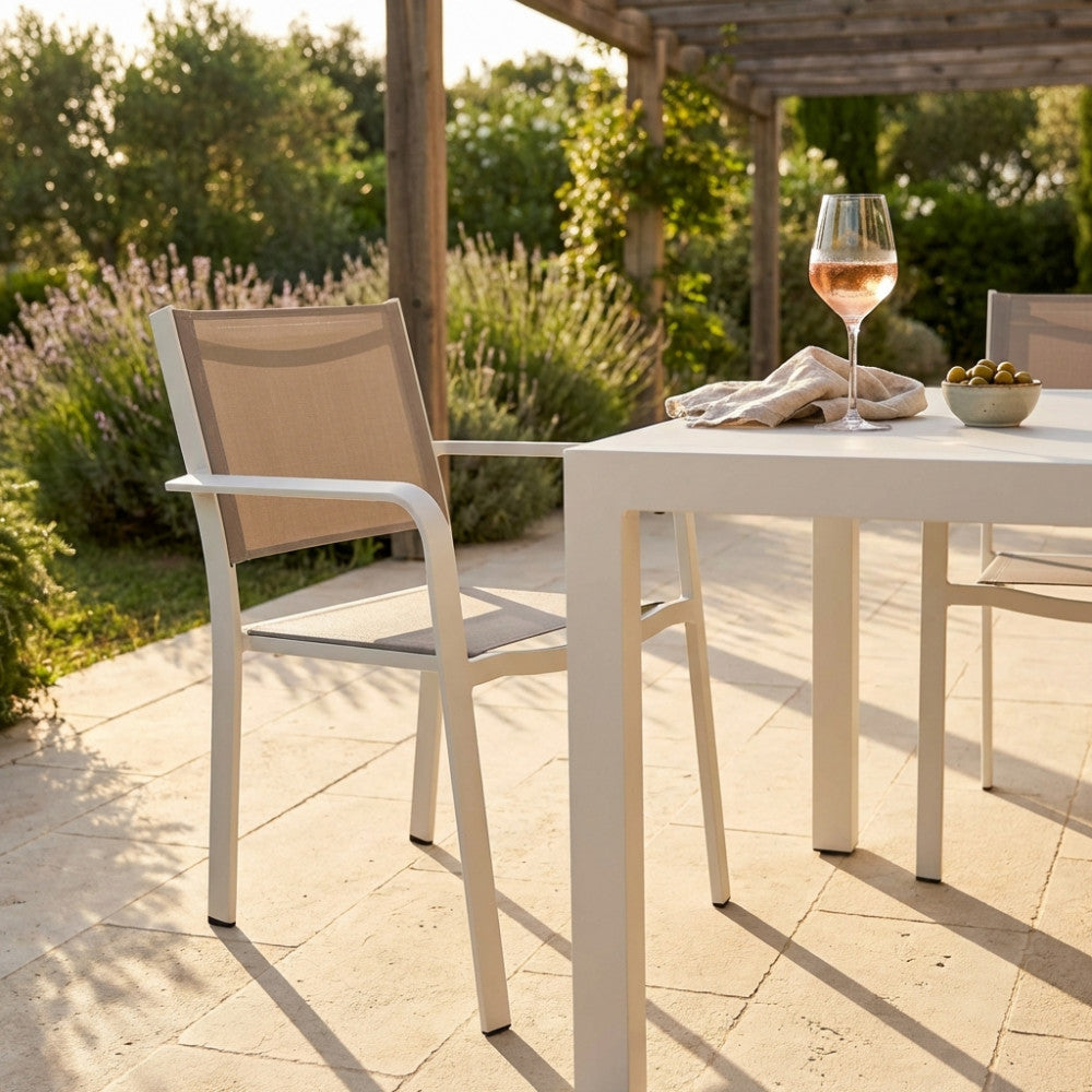 Poltrona Zante in alluminio e textilene color tortora, ambientata all'aperto accanto a un tavolo bianco con un calice di vino.