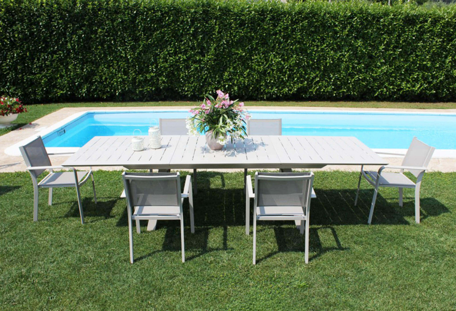 Set da pranzo outdoor composto da un lungo tavolo bianco e sei poltrone Zante in textilene tortora, a bordo piscina.