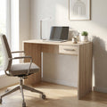 Scrivania Tom in quercia chiaro ambientata in un luminoso angolo studio con sedia ergonomica e portatile.