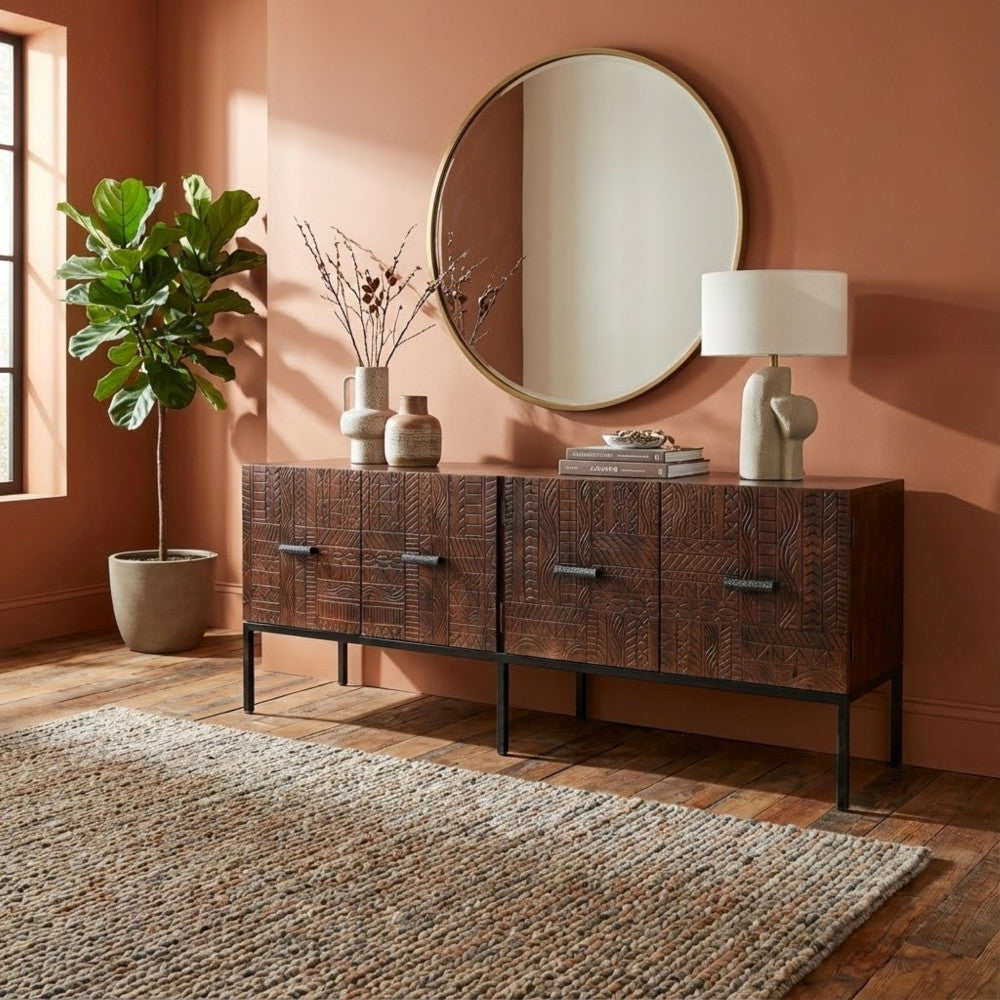 Ambientazione elegante con il porta TV Dominick sormontato da uno specchio rotondo, lampada scultorea e pianta d'appartamento su sfondo terracotta.
