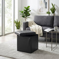 Pouf contenitore quadrato in ecopelle nera con coperchio semiaperto, posizionato su un tappeto chiaro accanto a un divano grigio in un salotto luminoso.