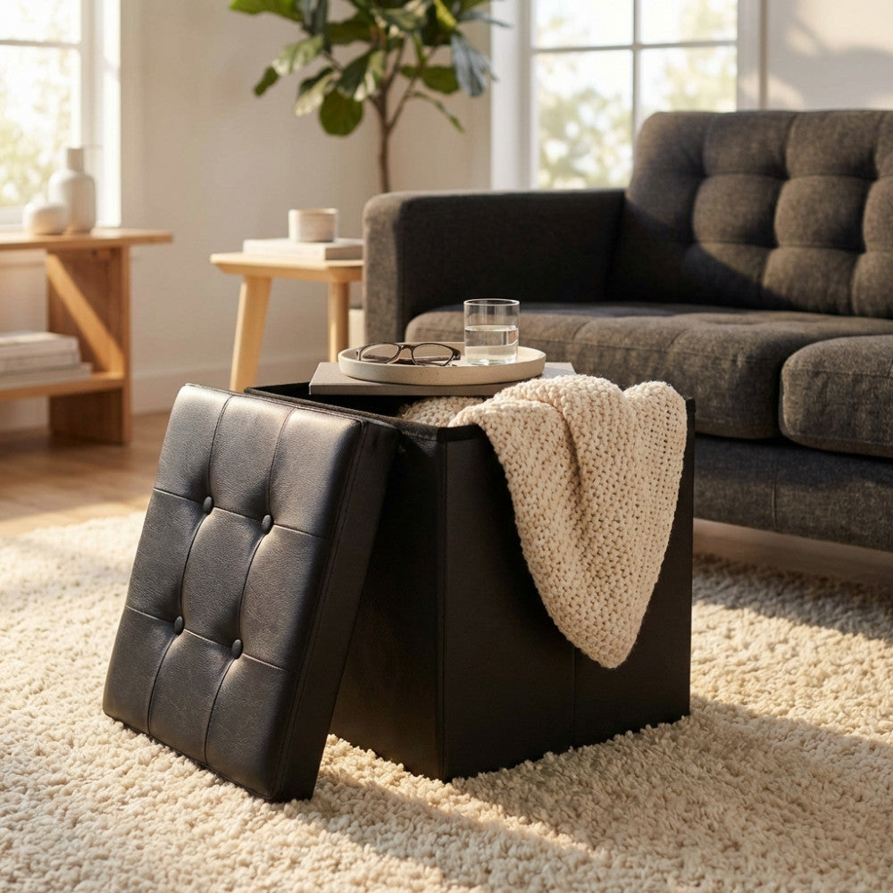 Pouf contenitore in ecopelle nera aperto, con una coperta in maglia chiara all'interno, situato in un elegante ambiente living moderno.