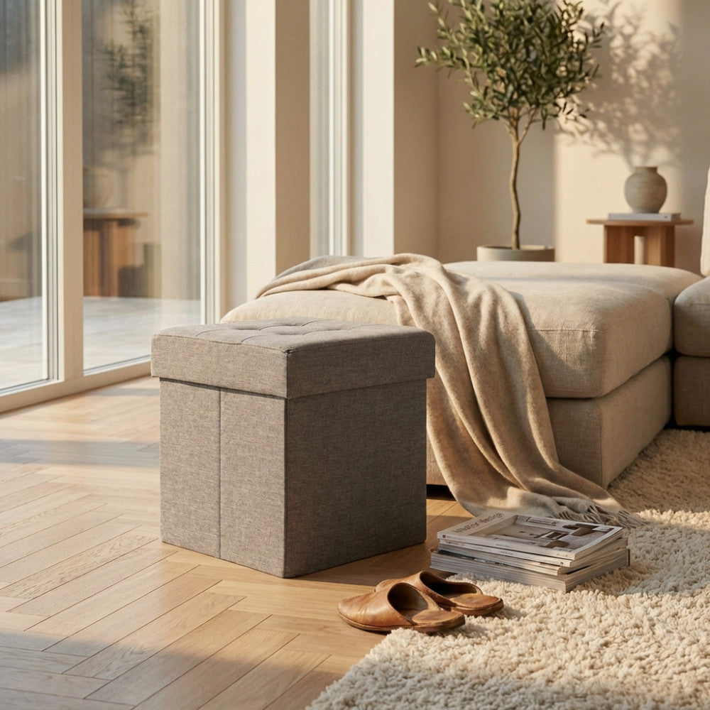 Pouf contenitore quadrato in tessuto grigio chiaro ambientato in un luminoso soggiorno moderno con pavimento in parquet.