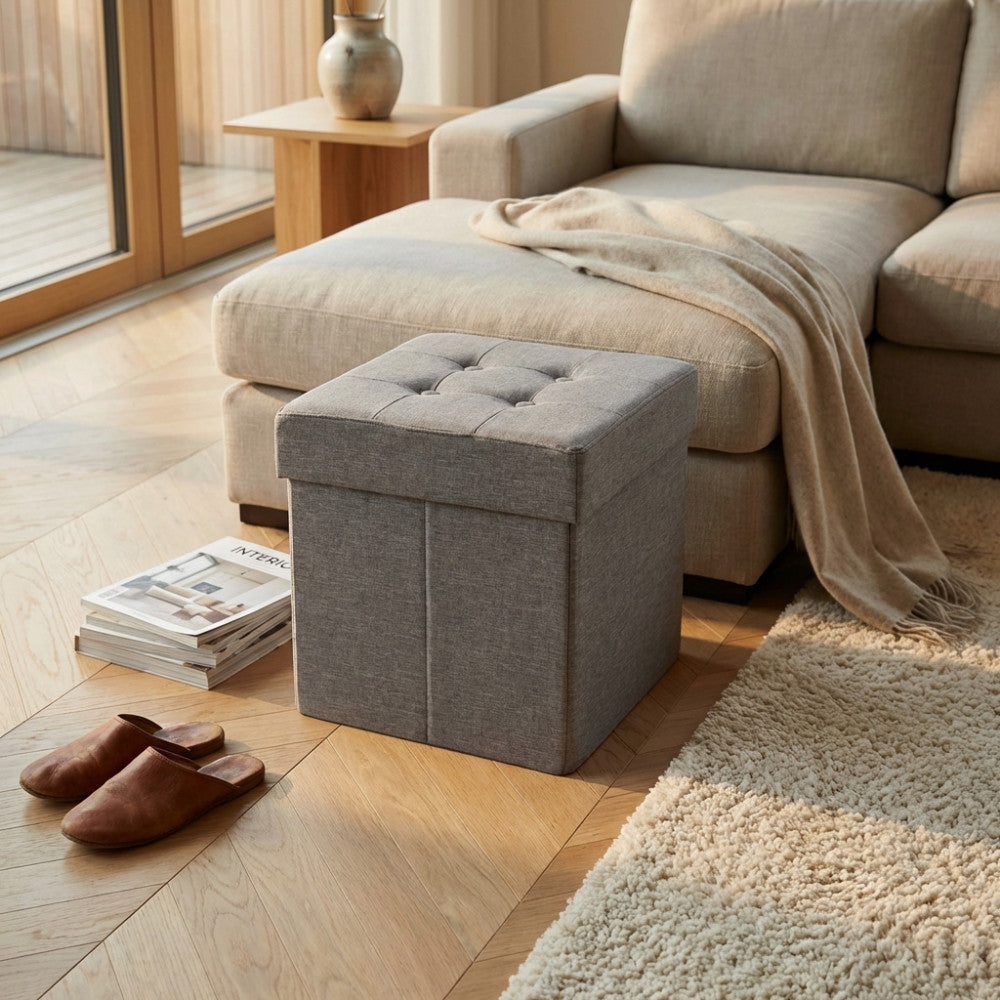 Dettaglio del pouf contenitore grigio posizionato accanto a un divano beige con una coperta in morbido filato.