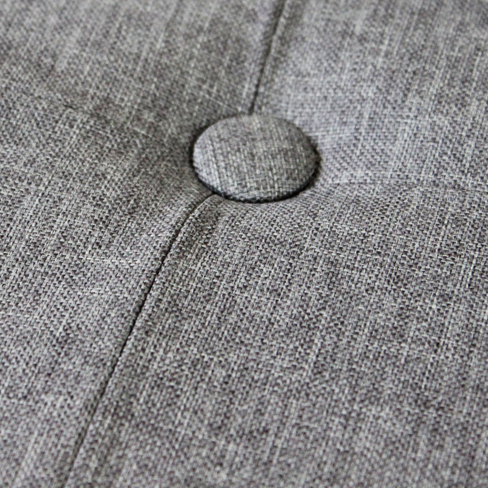 Primo piano della lavorazione capitonné con bottone centrale sul rivestimento in tessuto grigio del pouf.