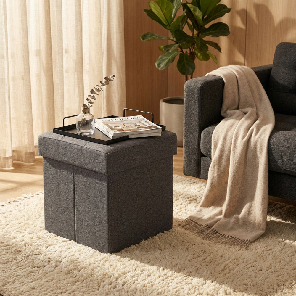 Pouf contenitore in tessuto grigio scuro allestito come tavolino da salotto con vassoio e riviste.