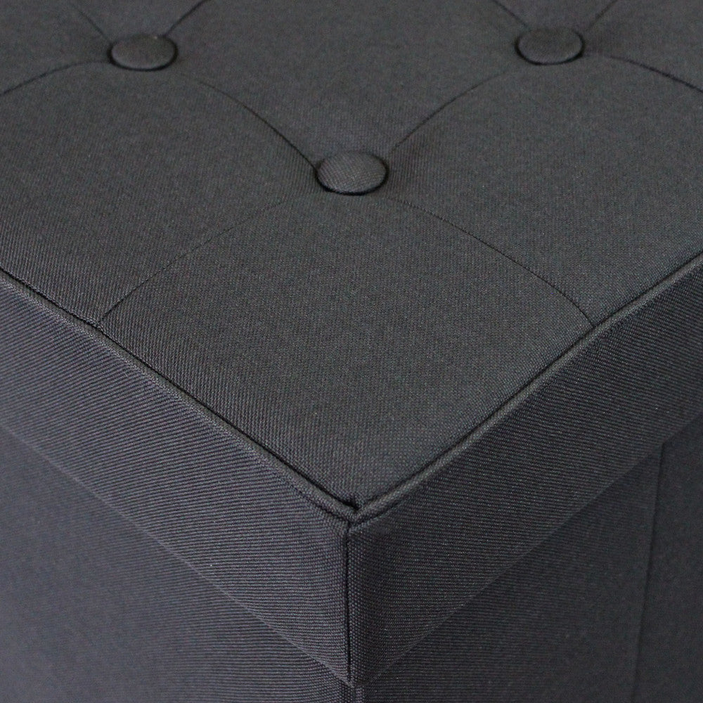 Dettaglio delle cuciture angolari e della texture materica del tessuto sul pouf nero.