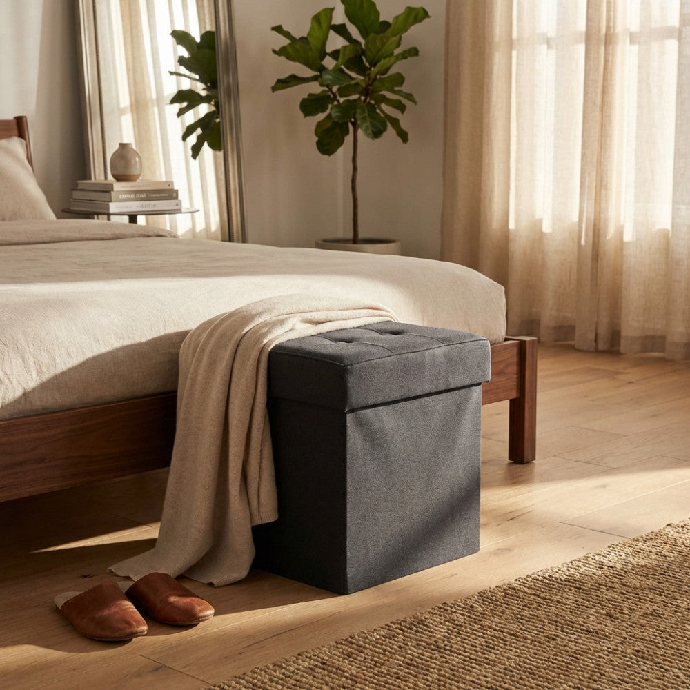 Pouf contenitore nero posizionato ai piedi di un letto in una camera da letto luminosa.