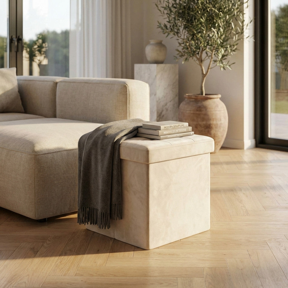 Pouf contenitore quadrato in velluto beige utilizzato come tavolino con libri in un soggiorno luminoso.