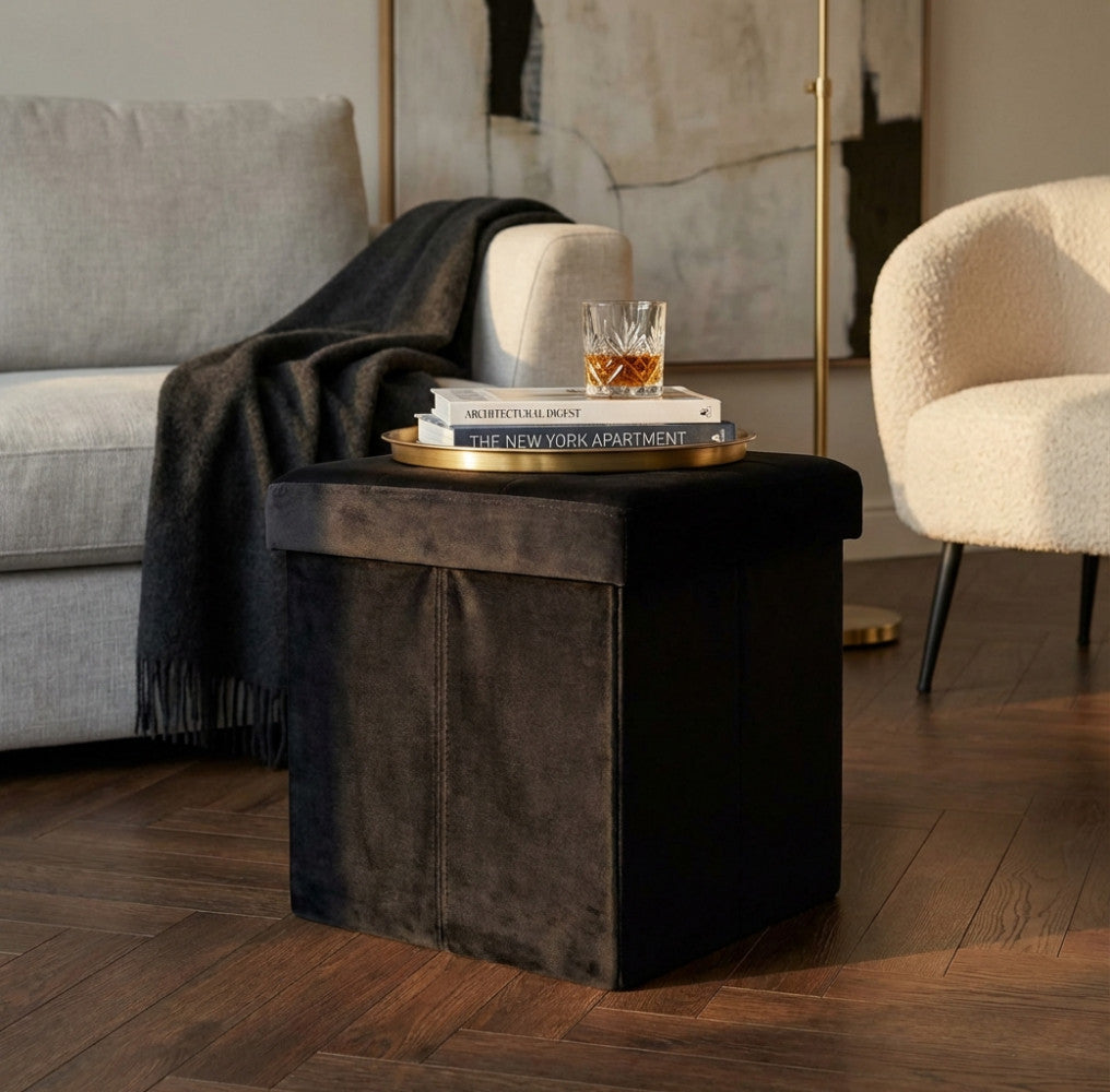 Pouf contenitore in velluto nero ambientato in un salotto elegante con vassoio dorato e bicchiere in cristallo.