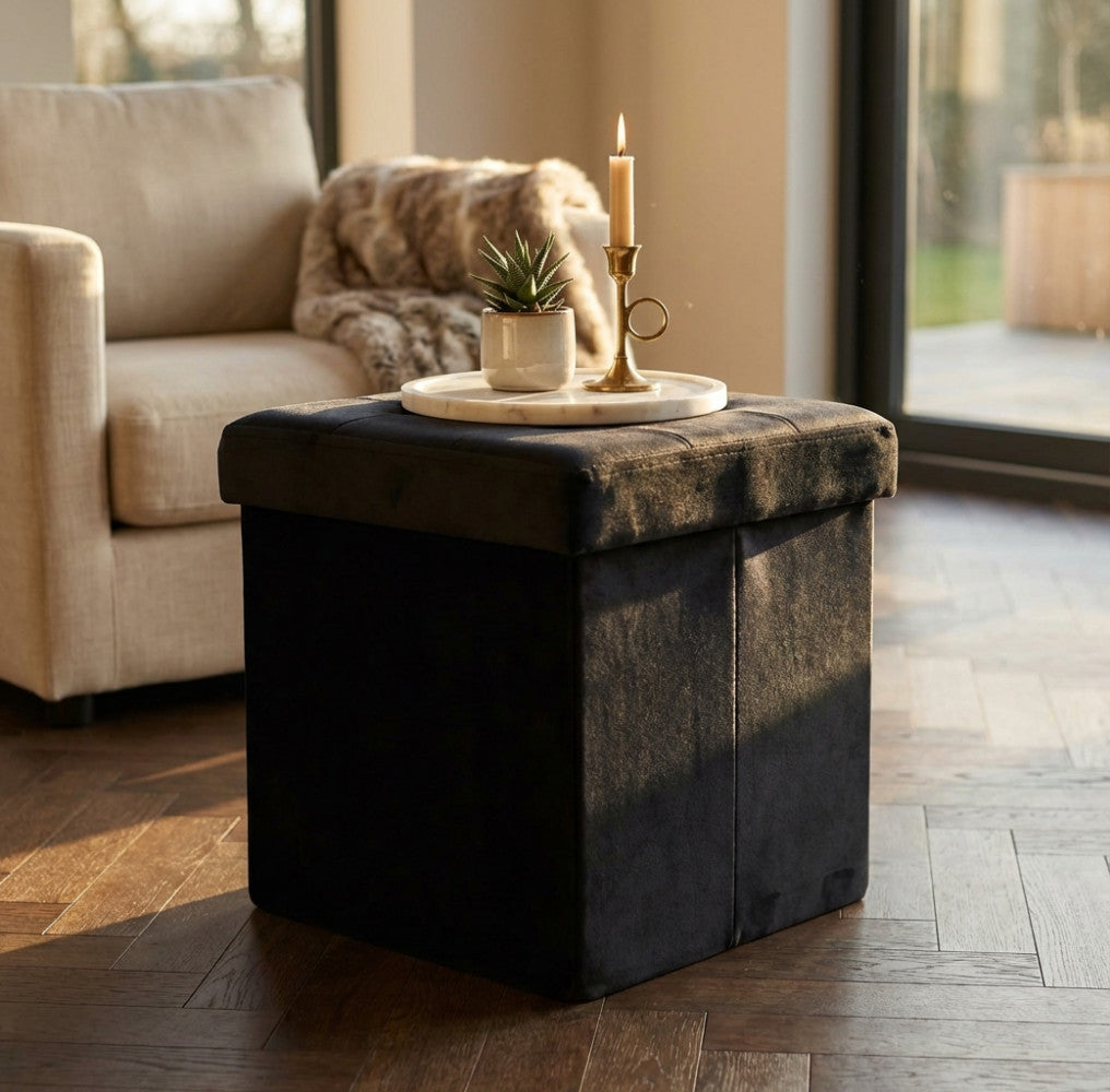 Pouf quadrato nero utilizzato come tavolino da salotto con vassoio in marmo, candela e piccola pianta.