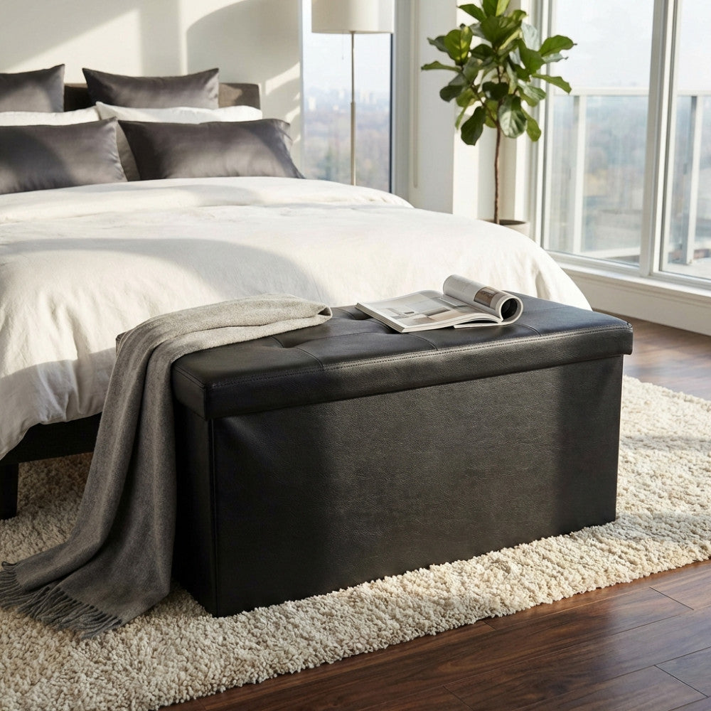 Pouf contenitore rettangolare nero posizionato ai piedi di un letto in una camera da letto moderna e luminosa.