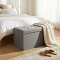 Pouf contenitore rettangolare in tessuto grigio posizionato ai piedi di un letto in una camera luminosa.