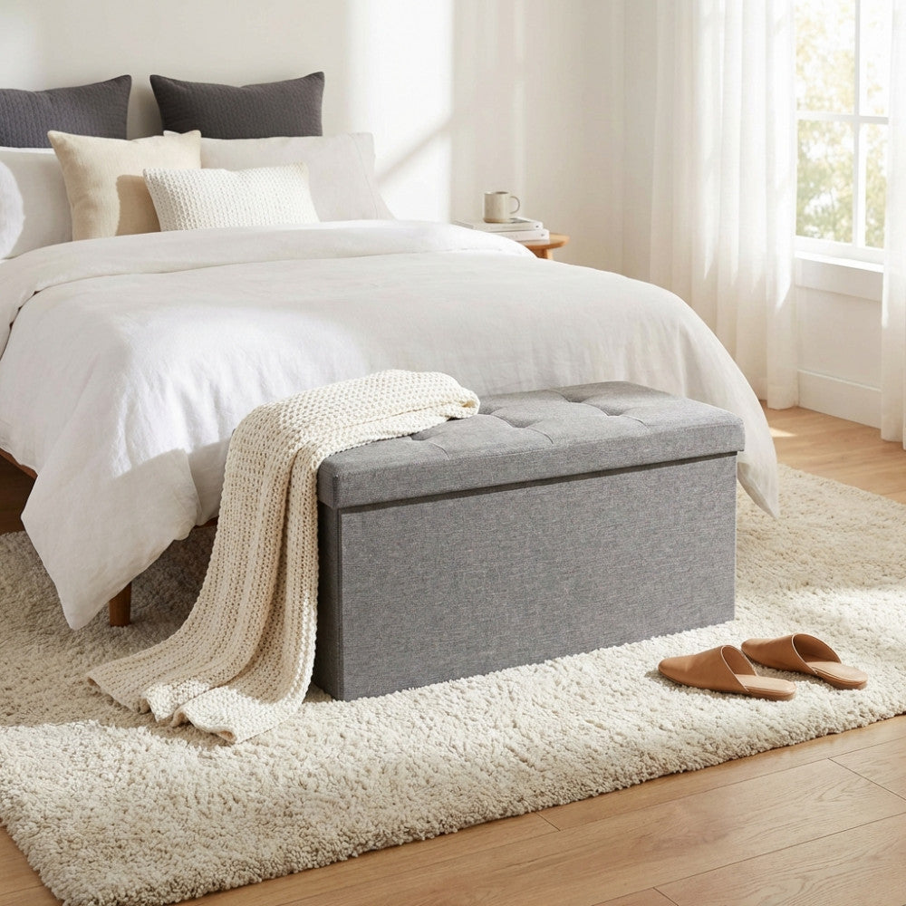 Vista angolare del pouf contenitore grigio in tessuto, integrato in una camera da letto dai toni neutri.