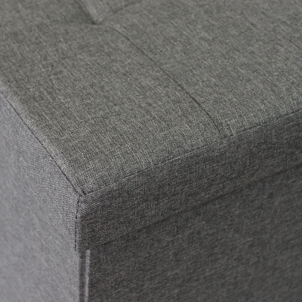 Primo piano dell'angolo del pouf, che mette in risalto le cuciture sartoriali e la trama materica del tessuto grigio scuro.