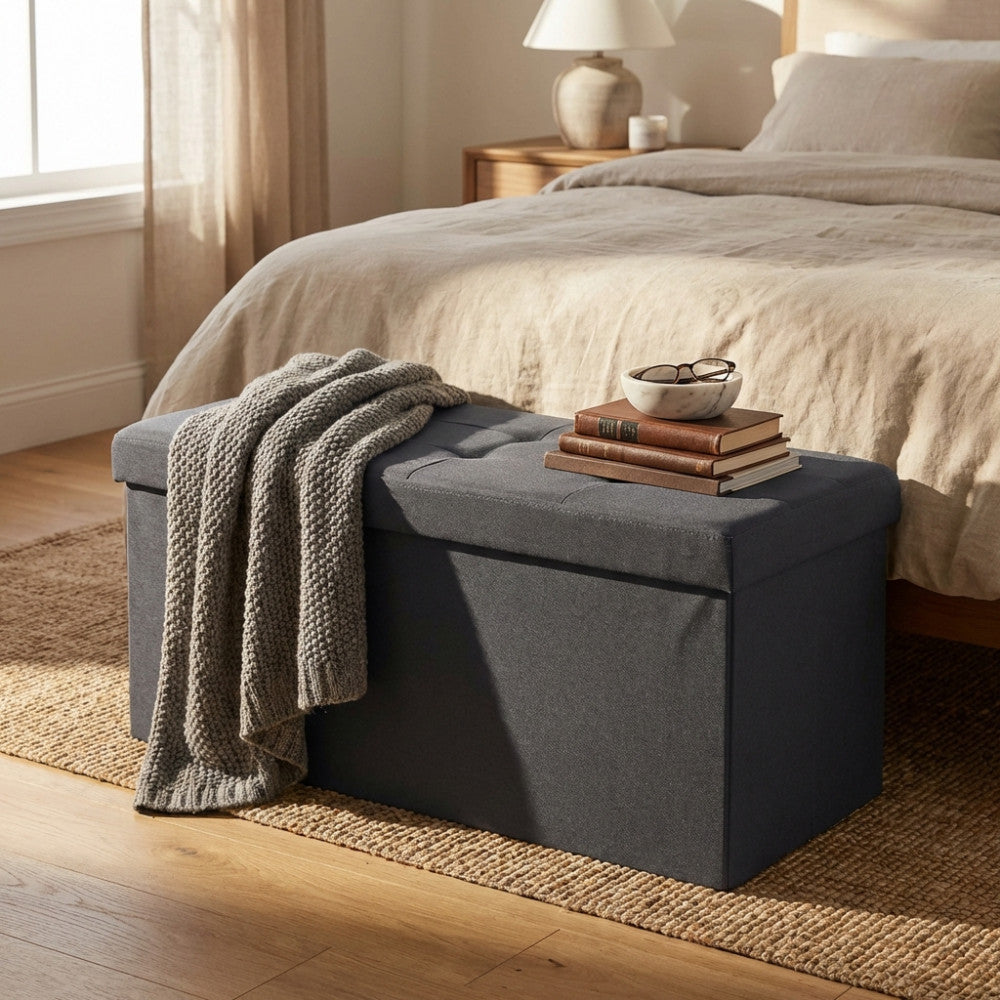 Dettaglio del pouf contenitore nero utilizzato come piano d'appoggio per libri e una coperta in maglia nel living.
