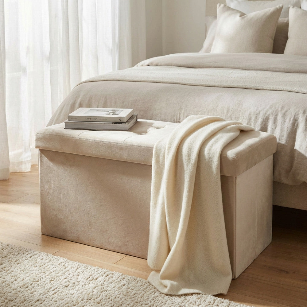 Pouf contenitore in velluto beige posizionato ai piedi di un letto con una morbida coperta chiara.