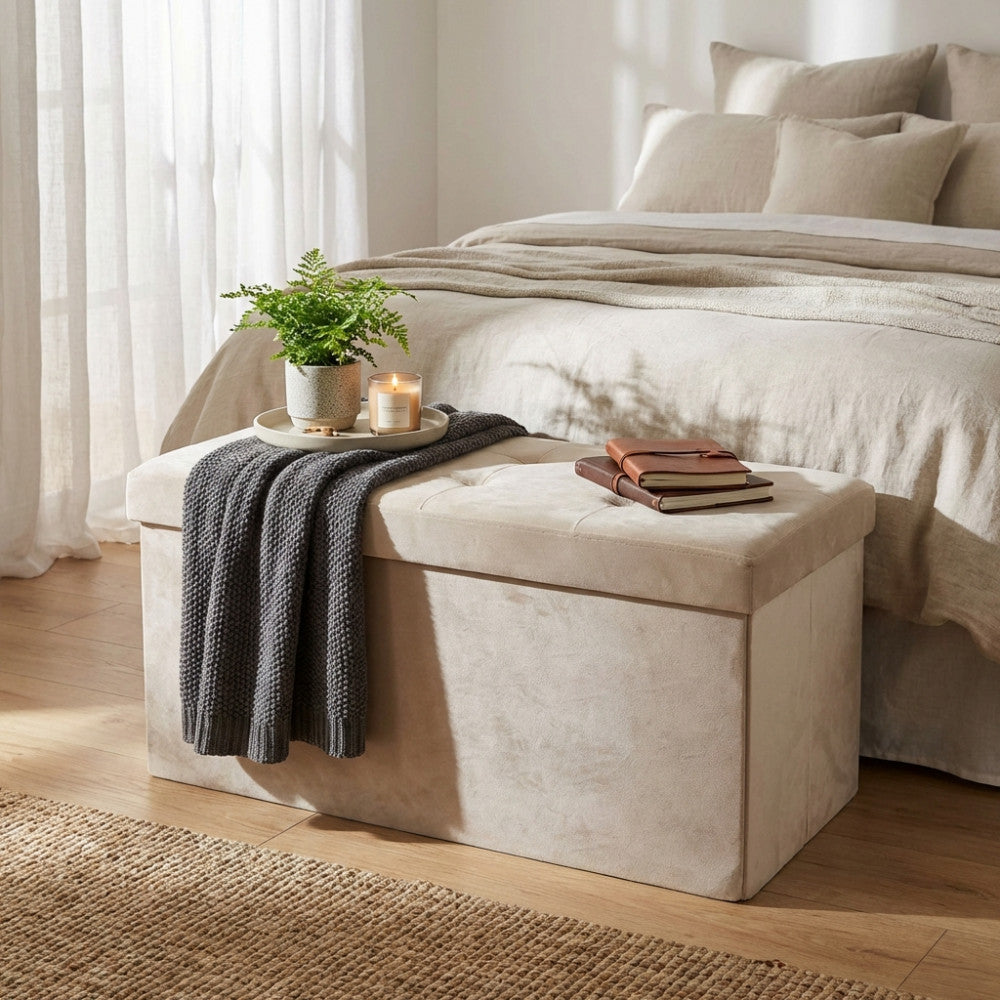 Pouf rettangolare in velluto beige allestito con vassoio, candela, pianta e libri in una camera da letto elegante.