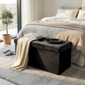 Pouf contenitore in velluto nero posizionato ai piedi di un letto matrimoniale con coperta chiara e vassoio decorativo.