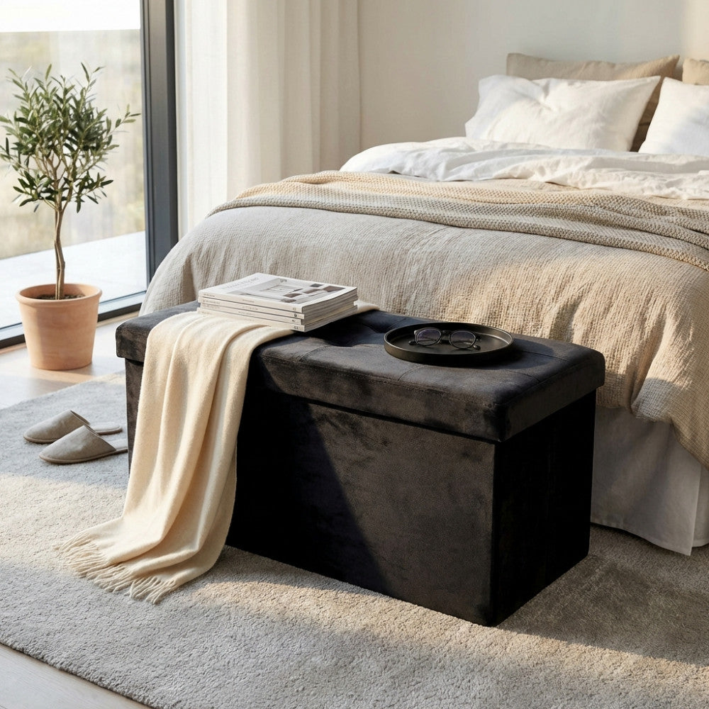 Pouf contenitore in velluto nero posizionato ai piedi di un letto matrimoniale con coperta chiara e vassoio decorativo.