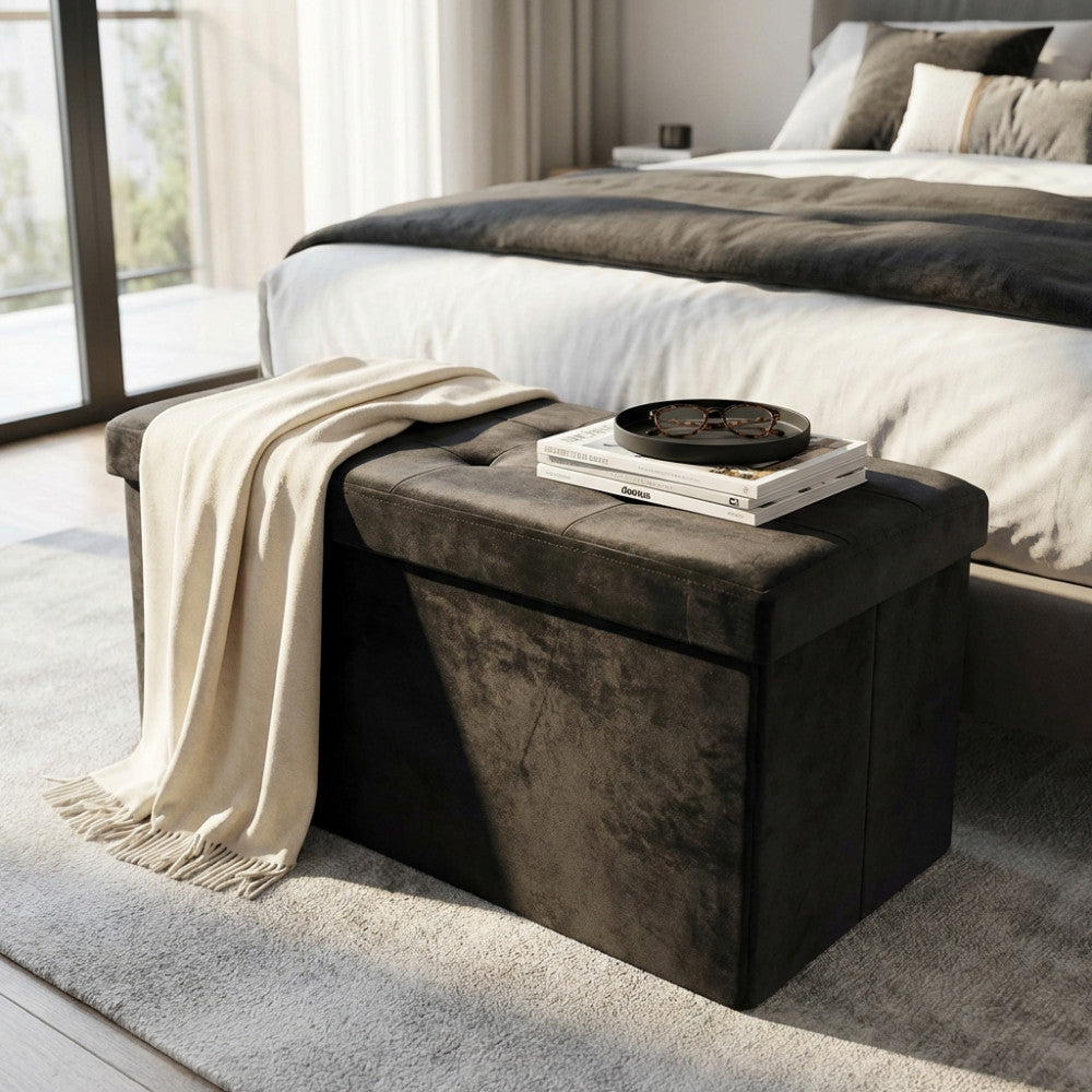 Vista angolata del pouf contenitore in velluto nero in una camera da letto luminosa, arricchito da un plaid e riviste.