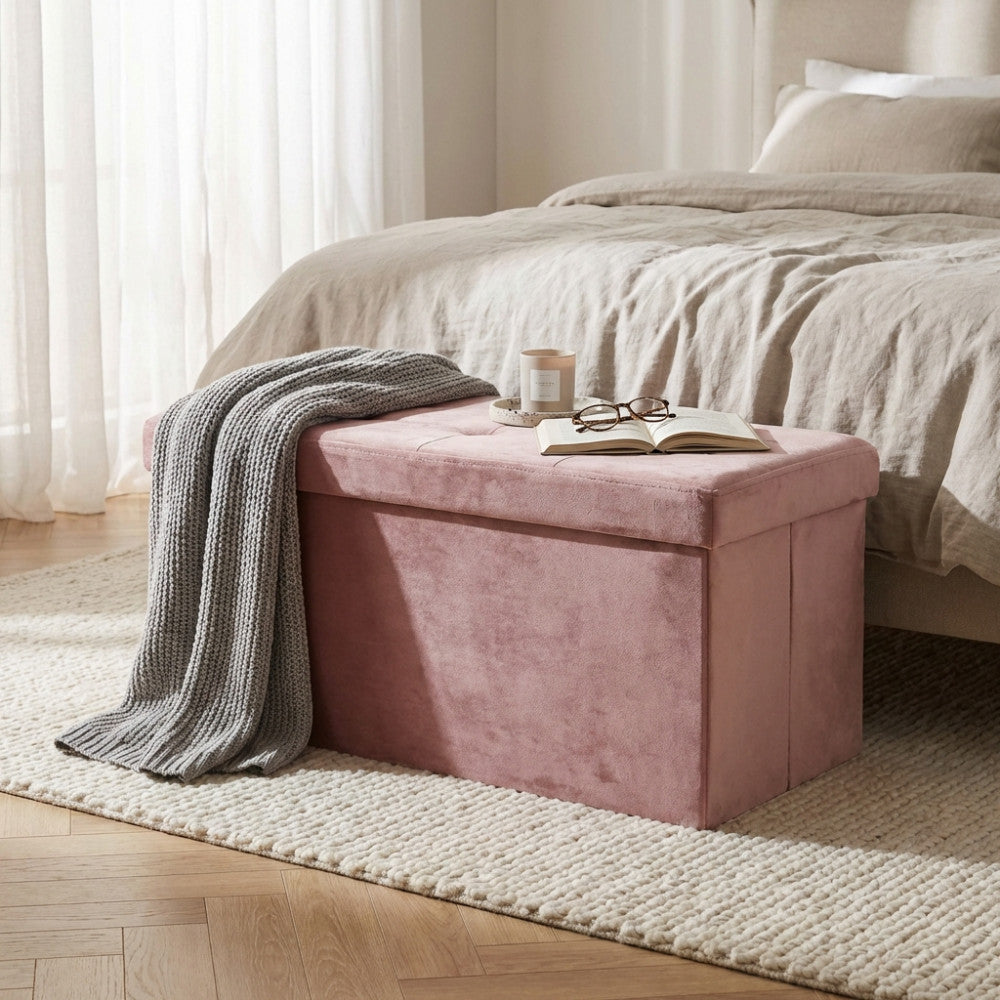 Dettaglio del pouf contenitore in velluto rosa in un ambiente camera da letto, decorato con una candela, occhiali e un libro aperto.