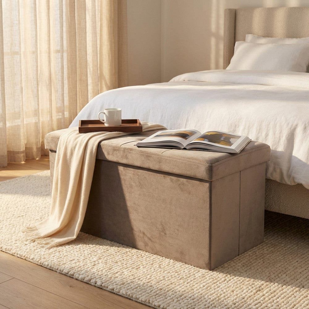 Pouf contenitore rettangolare in velluto tortora posizionato ai piedi di un letto matrimoniale, illuminato dalla luce naturale.