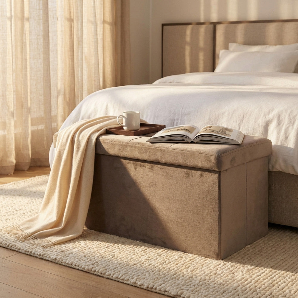 Dettaglio del pouf contenitore in velluto tortora in una camera da letto elegante, con un vassoio in legno e una coperta chiara.