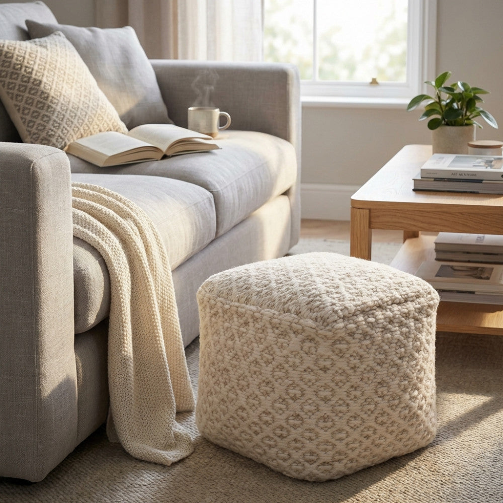 Pouf Jean in lana e cotone bianco ecrù posizionato accanto a un divano grigio in un luminoso soggiorno moderno.