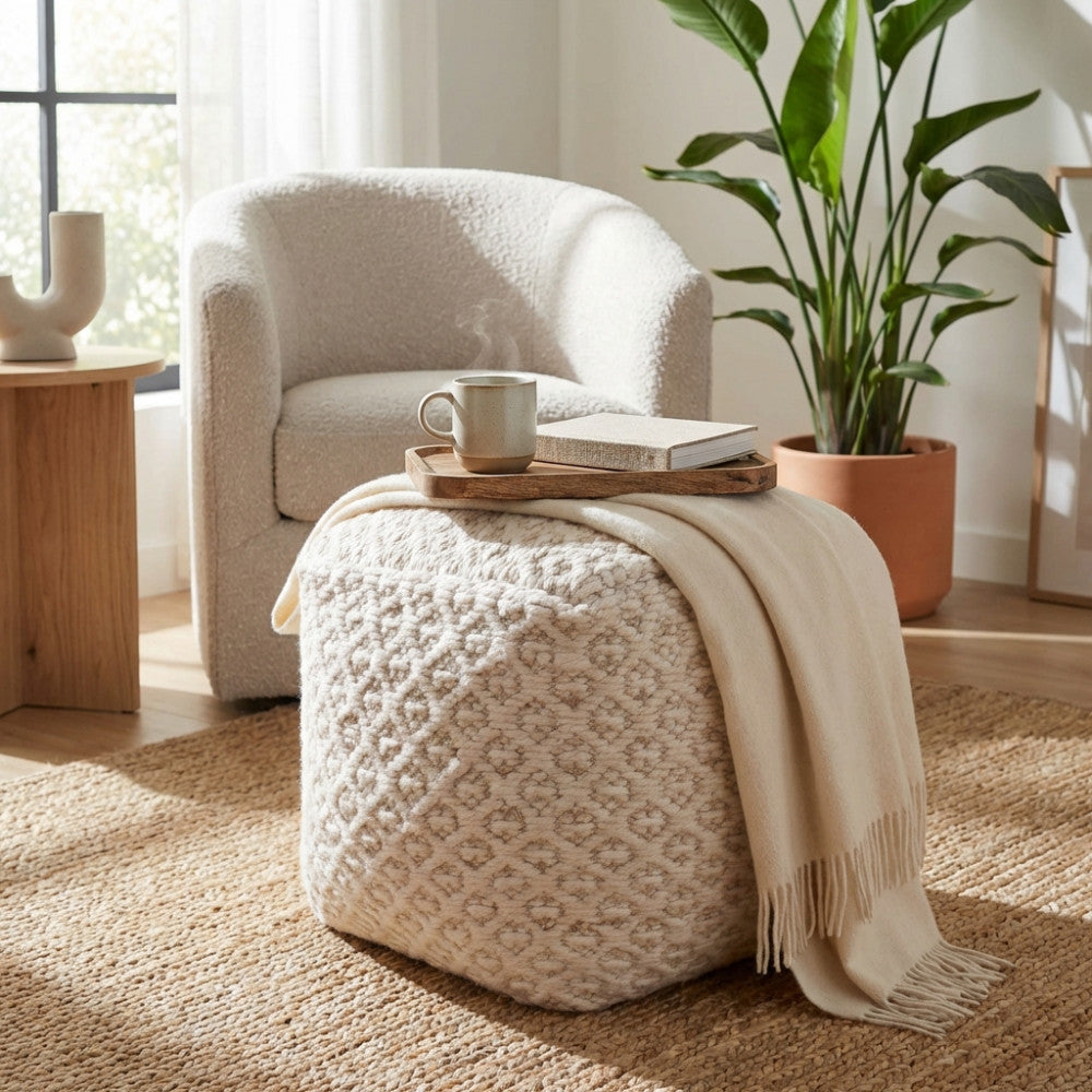Pouf Jean utilizzato come tavolino con vassoio in legno, accanto a una poltrona bouclé e una pianta d'appartamento.