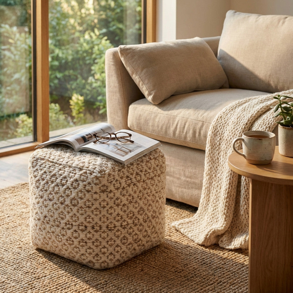 Pouf JEAN in lana e juta posizionato su un tappeto in fibre naturali accanto a un divano beige, con una rivista aperta sopra.