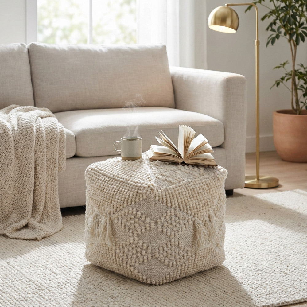 Pouf Jildaz in lana e cotone bianco posizionato in un soggiorno luminoso accanto a un divano neutro, arricchito da un libro e una tazza.