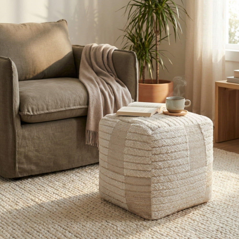Pouf Josselin utilizzato come elegante piano d'appoggio con un libro e una tazza, affiancato a una poltrona moderna.