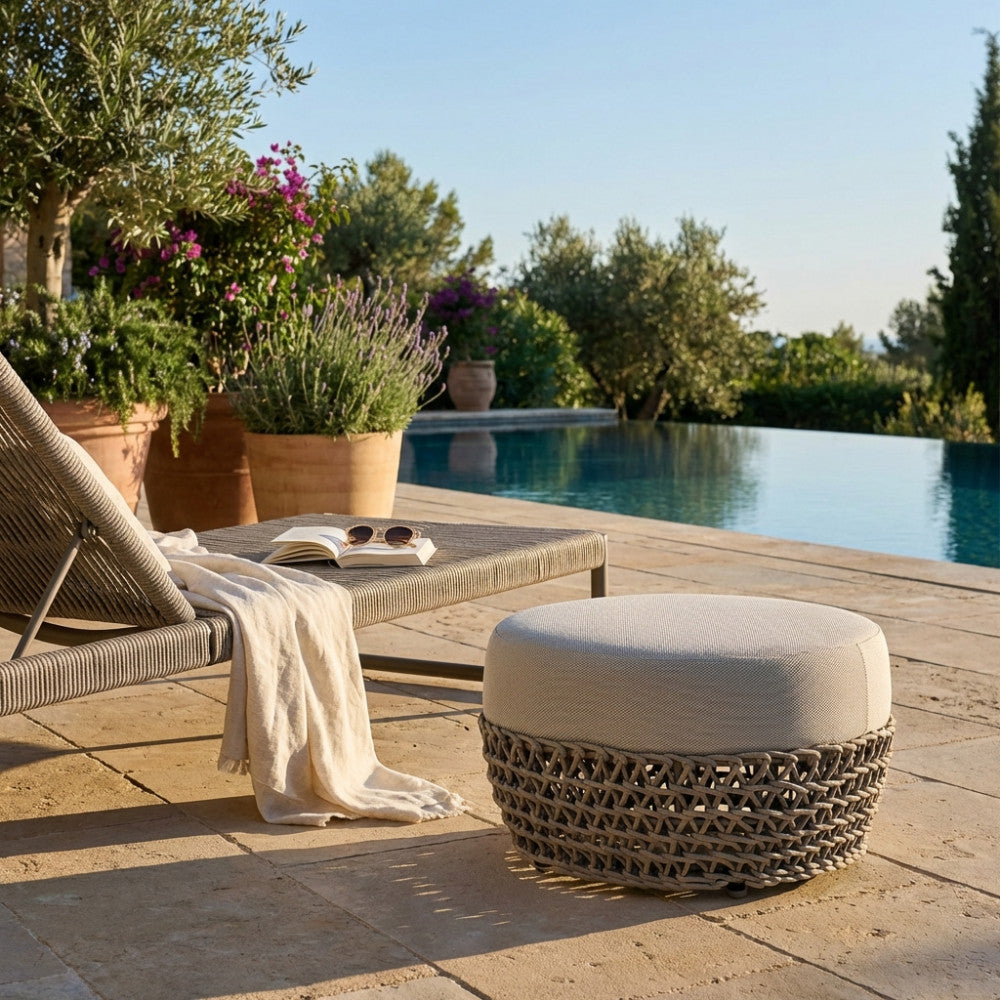 Pouf Lafayette beige in corda e alluminio posizionato a bordo piscina accanto a un lettino prendisole.