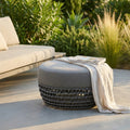 Pouf Lafayette grigio in corda e alluminio ambientato in un giardino moderno al tramonto.