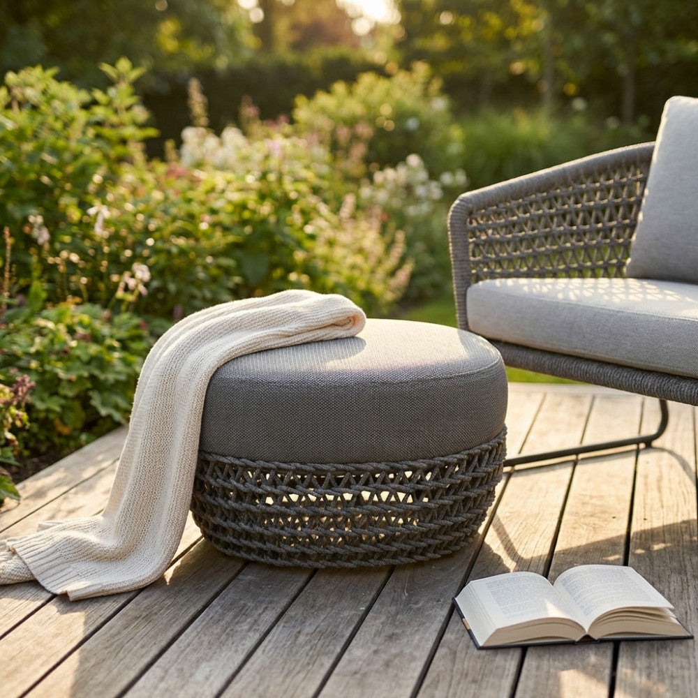 Dettaglio del pouf Lafayette con coperta in maglia appoggiata, su una terrazza in legno.
