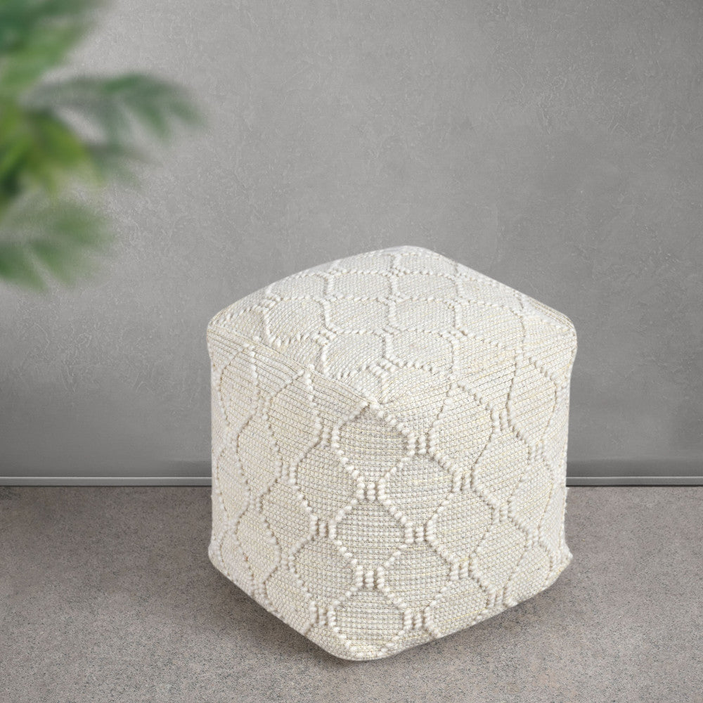 Pouf Méliton in lana e juta bianca ambientato in uno spazio minimalista con pavimento in pietra e parete grigia.