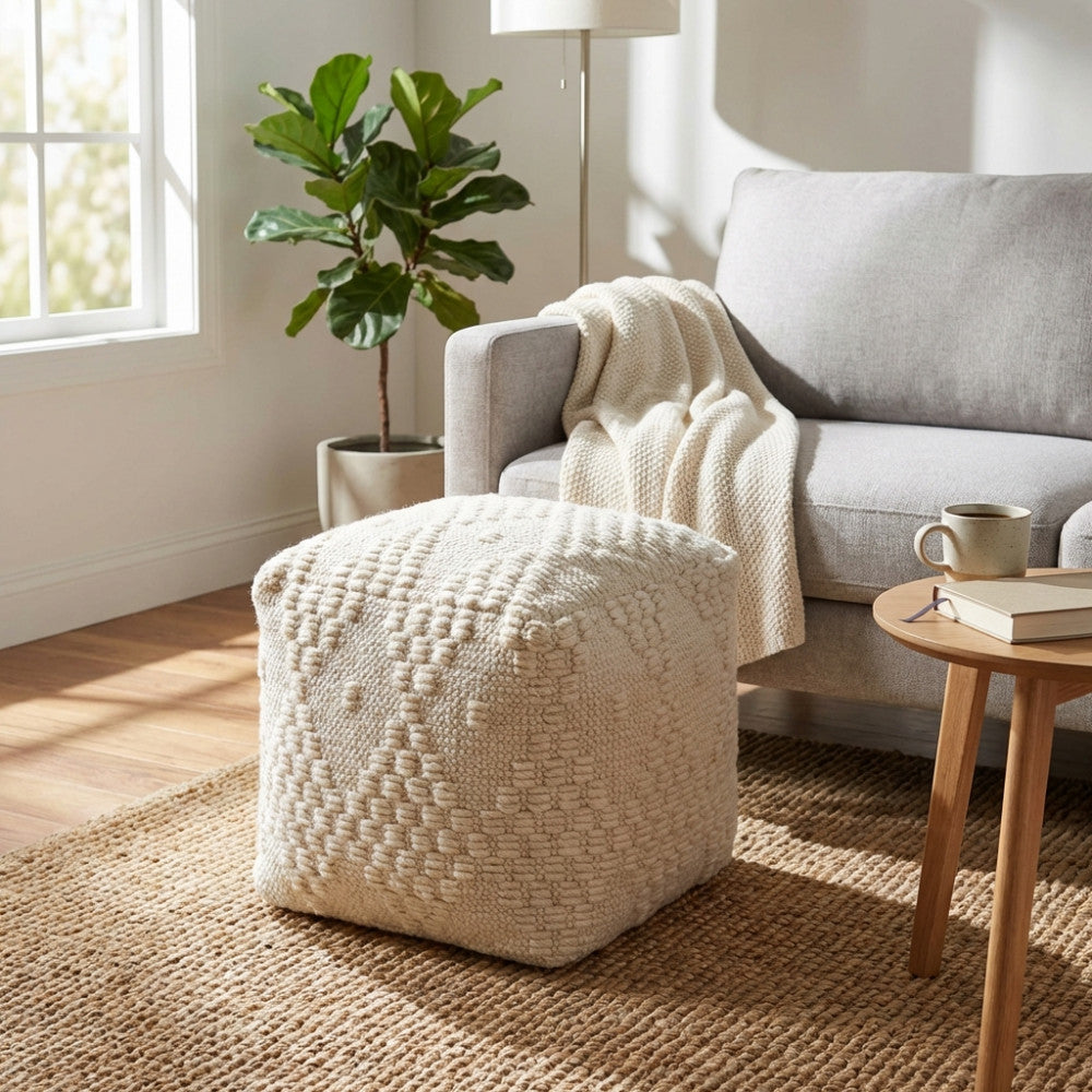 Pouf moderno bianco materico appoggiato su un tappeto in iuta naturale accanto a un divano contemporaneo con un plaid in maglia.