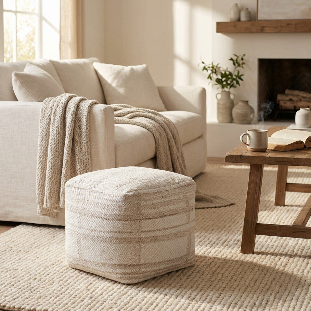 Pouf Mathis in lana e cotone bianco ecrù ambientato in un salotto luminoso accanto a un divano chiaro.