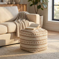 Pouf quadrato Nicolas in cotone e lana bianco e marrone chiaro, ambientato in un soggiorno luminoso accanto a un divano beige con un libro aperto sopra.